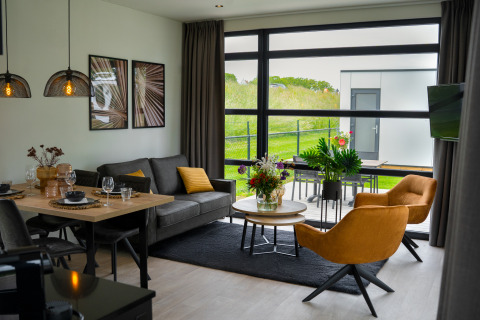 Moderne woonkamer in Villa Maritiem met grote ramen, eethoek en uitzicht op het groene buitengebied.