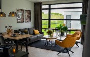 Salón moderno en la Villa Maritiem con grandes ventanales, comedor y vistas a zonas verdes exteriores.