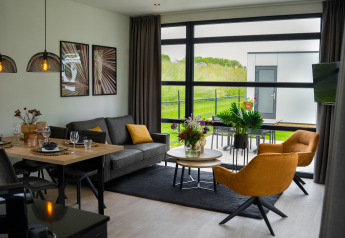 Moderne woonkamer in Villa Maritiem met grote ramen, eethoek en uitzicht op het groene buitengebied.