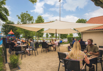 Comedor al aire libre en Villa Maritiem, huéspedes disfrutan comidas bajo toldos cerca de un parque infantil.