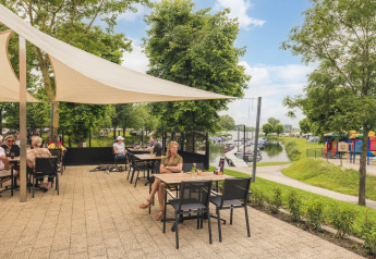 Terraza exterior de Villa Maritiem con invitados, vista al puerto deportivo y parque infantil en un día soleado.