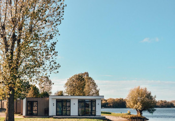 Modern lodge at the water's edge in MarinaPark Bad Nederrijn, Netherlands, surrounded by trees and lake.