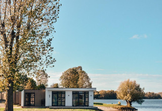 Lodge moderno junto al agua en MarinaPark Bad Nederrijn, Países Bajos, rodeado de árboles y lago tranquilo.