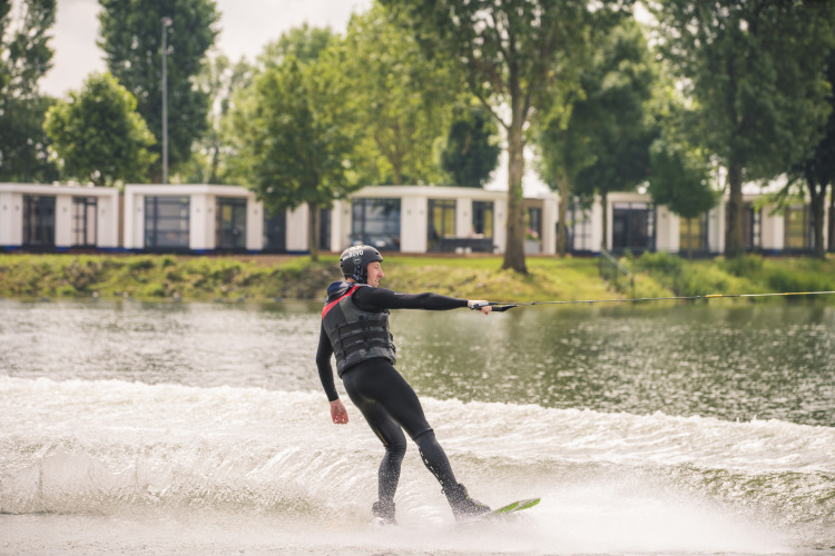 Iemand doet aan wakeboarden op een meer bij lodge Villa Maritiem, omgeven door bomen en chalets.