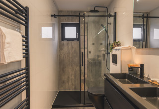 Baño moderno en Villa Maritiem con accesorios negros, ducha efecto lluvia y radiador toallero negro.