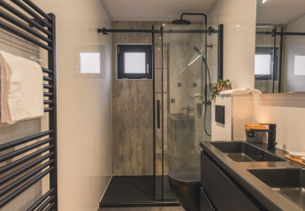 Baño moderno en Villa Maritiem con accesorios negros, ducha efecto lluvia y radiador toallero negro.
