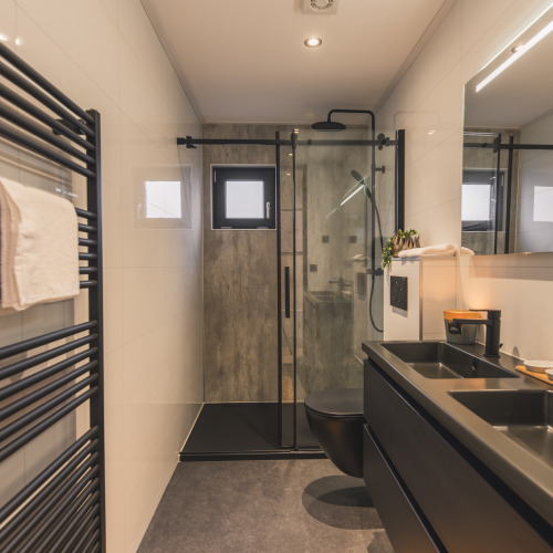 Baño moderno en Villa Maritiem con accesorios negros, ducha efecto lluvia y radiador toallero negro.