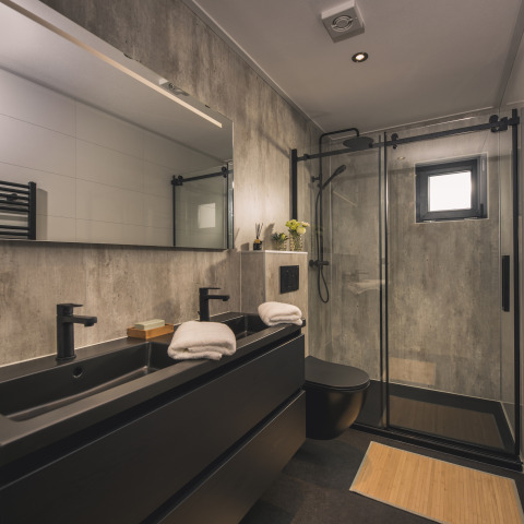 Baño moderno en la Villa Maritiem lodge con lavabo doble negro, ducha de vidrio y toallas blancas.