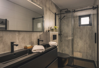 Salle de bain moderne à la Villa Maritiem lodge avec double vasque noire, douche en verre et serviettes.
