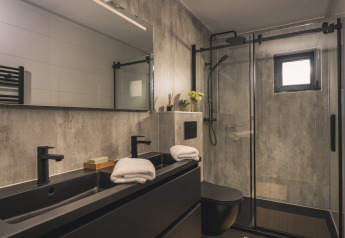 Salle de bain moderne à la Villa Maritiem lodge avec double vasque noire, douche en verre et serviettes.