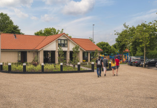 Cuatro personas caminan hacia la Villa Maritiem en MarinaPark Bad Nederrijn, Países Bajos, con parque infantil cercano.