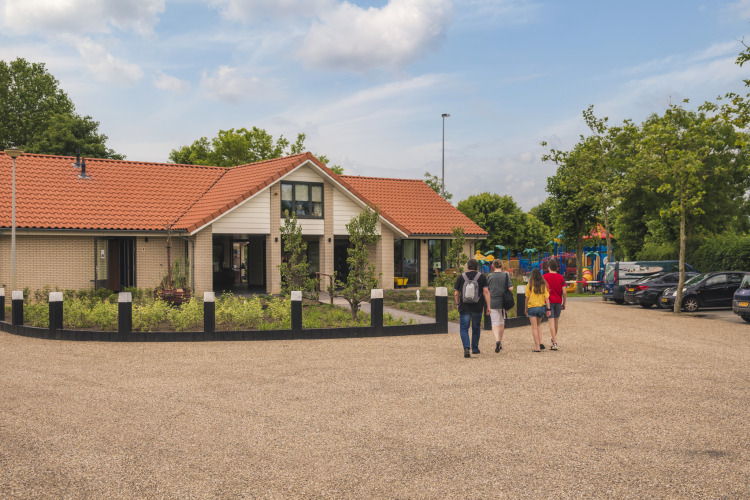 Vier mensen lopen bij Villa Maritiem lodge op MarinaPark Bad Nederrijn in Nederland, met speeltuin op de achtergrond.