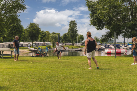 Quattro adulti giocano a badminton sul prato vicino all'acqua a Villa Maritiem, MarinaPark Bad Nederrijn, Paesi Bassi.