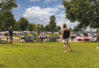 Cuatro adultos juegan bádminton en el césped junto al agua en Villa Maritiem, MarinaPark Bad Nederrijn, Países Bajos.