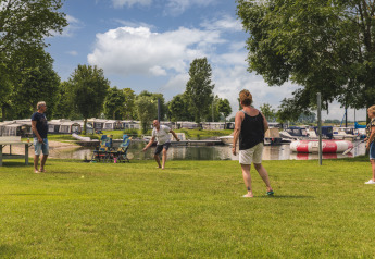 Cuatro adultos juegan bádminton en el césped junto al agua en Villa Maritiem, MarinaPark Bad Nederrijn, Países Bajos.