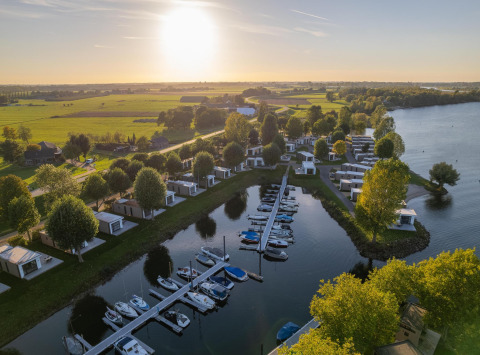 Vista aerea di Villa Maritiem lodge con barche, casette moderne, prati verdi e un tramonto sul lago.