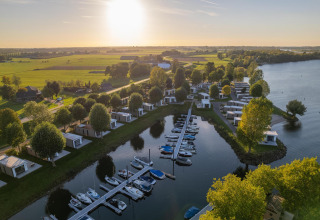 Luchtfoto van Villa Maritiem lodge met boten, moderne chalets, veel groen en uitzicht op het meer bij zonsondergang.