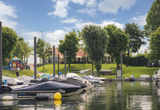 Barcos atracados en la marina cerca de Villa Maritiem, con césped, árboles y parque infantil al fondo.