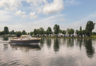 Una lancha navega junto a modernas villas junto al lago Villa Maritiem, rodeadas de árboles y bajo cielo azul.