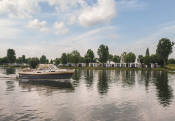Una lancha navega junto a modernas villas junto al lago Villa Maritiem, rodeadas de árboles y bajo cielo azul.