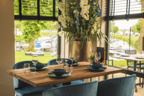 Mesa en Villa Maritiem Lodge, elegantemente puesta junto a grandes ventanas con vista a un puerto de botes.