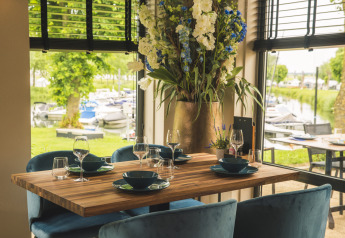 Mesa en Villa Maritiem Lodge, elegantemente puesta junto a grandes ventanas con vista a un puerto de botes.