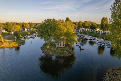 Luxe glampingverblijf op een klein eiland, omgeven door water, boten en groene natuur in het vakantiepark.