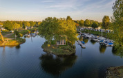 Luxe glampingverblijf op een klein eiland, omgeven door water, boten en groene natuur in het vakantiepark.