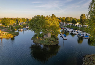 Luxe glamping-accommodatie op een eilandje, omgeven door water, boten en groene natuur in een vakantiepark.