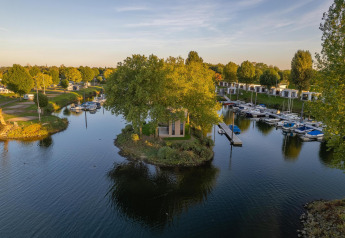 Luxe glamping-accommodatie op een eilandje, omgeven door water, boten en groene natuur in een vakantiepark.