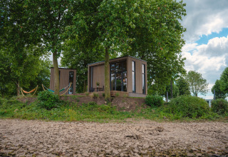 Tiny River House bij MarinaPark Bad Nederrijn in Nederland, omgeven door bomen, hangmatten en stenen