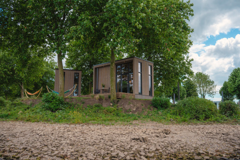 Tiny River House bij MarinaPark Bad Nederrijn in Nederland, omgeven door bomen, hangmatten en stenen