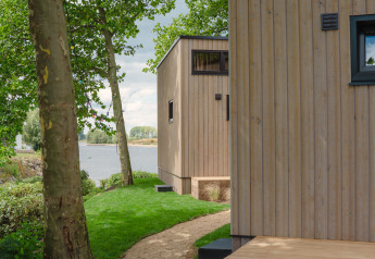 Pad langs houten tiny houses bij de rivier in MarinaPark Bad Nederrijn, Nederland, met groene bomen.