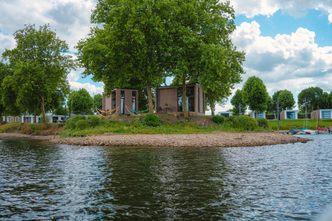 Tiny River House im MarinaPark Bad Nederrijn, Niederlande, umgeben von Bäumen und ruhigem Wasser.