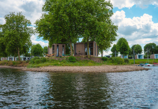Tiny River House im MarinaPark Bad Nederrijn, Niederlande, umgeben von Bäumen und ruhigem Wasser.