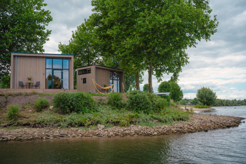 Tiny River House aan de oever in MarinaPark Bad Nederrijn, Nederland, omgeven door natuur en bomen.