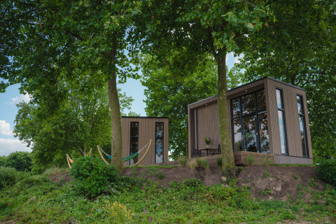 Moderne tiny house aan MarinaPark Bad Nederrijn in Nederland, omgeven door bomen en natuur.