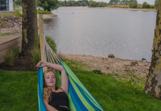 Jonge vrouw ontspant in een hangmat langs de rivier bij Tiny River House, MarinaPark Bad Nederrijn, Nederland.