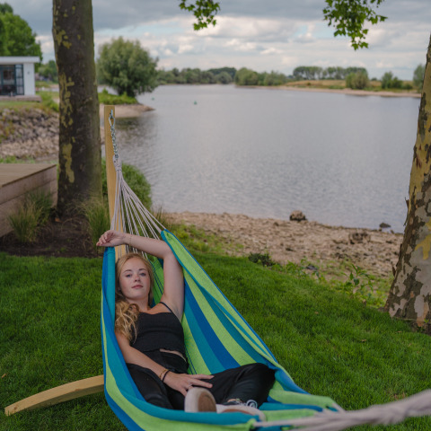 Jonge vrouw ontspant in een hangmat aan de rivier bij Tiny River House, MarinaPark Bad Nederrijn, Nederland.