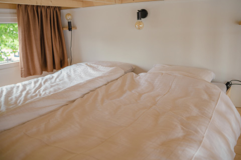 Acogedora zona de descanso con dos camas individuales y cortinas marrones en Tiny River House en los Países Bajos.