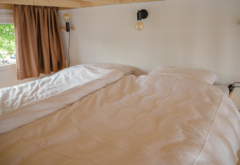 Acogedora zona de descanso con dos camas individuales y cortinas marrones en Tiny River House en los Países Bajos.
