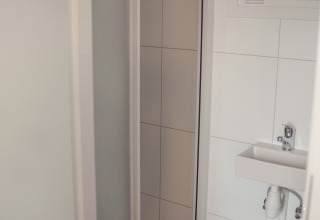 Pequeño baño en Tiny River House, Países Bajos, con azulejos blancos, lavabo y ventana con persianas.