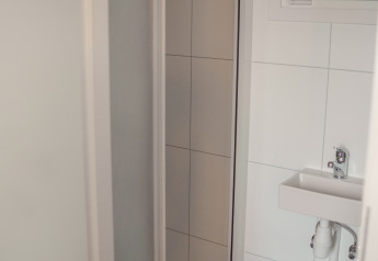 Kleine badkamer in Tiny River House, Nederland, met witte tegels, wasbak en raam met jaloezieën.