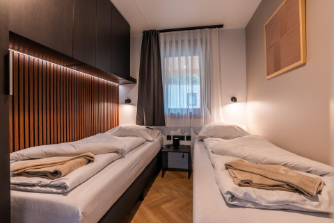 Chambre twin moderne avec panneaux bois et grande fenêtre au Wulfenia Waterfront, Ossiacher See, Autriche.