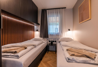 Chambre twin moderne avec panneaux bois et grande fenêtre au Wulfenia Waterfront, Ossiacher See, Autriche.