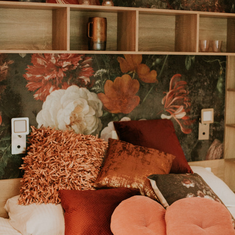 Luxuriöser Loftraum mit floraler Wand, gemusterten Kissen und offenen Regalen im Camping Si-Es-An, Niederlande.