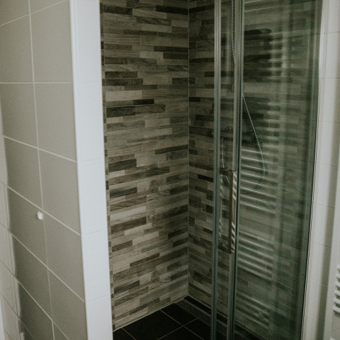 Modern shower with glass door and wood-style wall tiles in the Luxury Loft at Camping Si-Es-An, Netherlands.