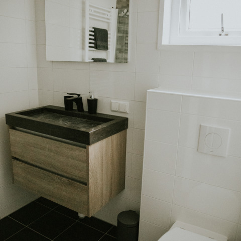 Baño moderno con lavabo negro, mueble de madera y azulejos blancos en Luxury loft, Camping Si-Es-An, Países Bajos.