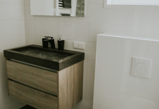 Salle de bain moderne avec lavabo noir, meuble en bois et carrelage blanc au Luxury loft, Camping Si-Es-An, Pays-Bas.
