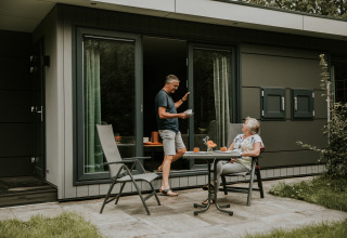 Pareja mayor disfruta café fuera de una tiny house de lujo en Camping Si-Es-An, Países Bajos.
